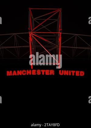 Dehors à Old Trafford la nuit. Stade Manchester United avec juste le logo rouge mis en évidence. Banque D'Images