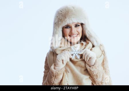 femme moderne souriante en manteau d'hiver et chapeau de fourrure isolé sur fond blanc dans des gants blancs avec flocon de neige. Banque D'Images