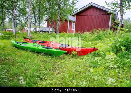 Deux kayaks - rouge et vert sont sur l'herbe verte, photo de côté bas niveau. Petit cottage au fond lointain Banque D'Images