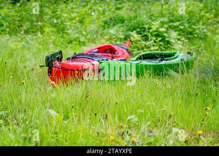 Deux kayaks intentionnellement flous - rouge et vert sont sur l'herbe verte. Gros plan photo de bas niveau. L'herbe de premier plan est mise au point Banque D'Images