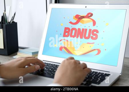 Gain de bonus. Femme utilisant un ordinateur portable avec à la table, closeup. Illustration de boîte cadeau ouverte, mot et confettis sur l'écran de l'appareil Banque D'Images