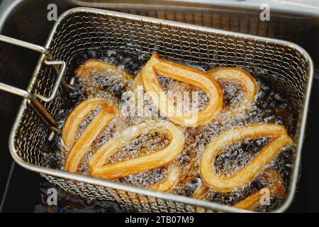 Les churros chauds et croquants sont sortis du panier de la friteuse après avoir été cuits dans l'huile. Les beignets dorés sont enrobés de sucre et de cannelle et font un Banque D'Images