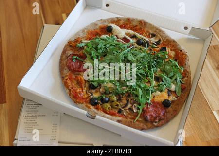 Délicieuse pizza avec roquette, champignons et olives dans une boîte sur une table en bois Banque D'Images