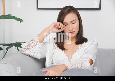 La femme dans la chemise de nuit en satin blanc a des démangeaisons autour de ses paupières en raison de réactions allergiques graves Banque D'Images