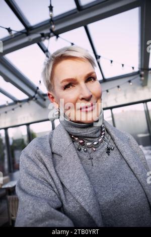 Gros plan portrait femme mature à la mode avec les cheveux blonds courts, dans des vêtements à la mode, captivant dans le col roulé gris élégant et veste, accessoire élégant Banque D'Images