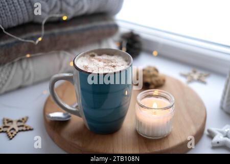 Nature morte de rebord de fenêtre d'hiver. Tasse en céramique bleue de café chaud sur le rebord de la fenêtre. Décorations de Noël sur le fond. Image de la maison confortable. Woolen k chaud Banque D'Images