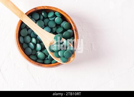 Gros plan de comprimés verts d'algues spirulines bénéfiques sur une cuillère en bois dans un bol en bois rempli de comprimés. Vue de dessus. Detox Banque D'Images