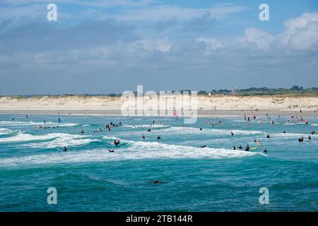 France, Plomeur, 2023-07-30. Plage de la torche avec de nombreux surfeurs au milieu des vagues océaniques et dunes de sable en arrière-plan. Banque D'Images