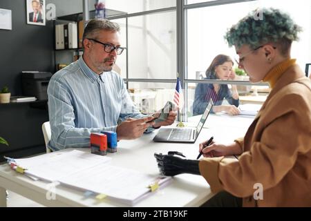 Femme handicapée ayant une réunion avec le gestionnaire dans le bureau tout en donnant des documents pour visa Banque D'Images