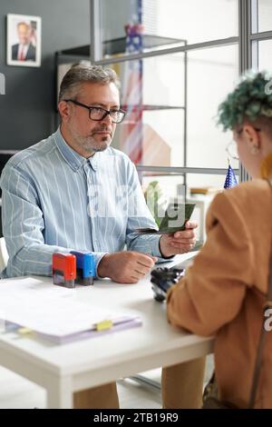 Image verticale du gestionnaire mature du centre de visa travaillant avec le client dans le bureau Banque D'Images