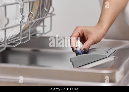 main féminine met la tablette de lave-vaisselle dans la machine lave-vaisselle intégrée automatique ouverte avec la vaisselle sale à l'intérieur. Gros plan Banque D'Images