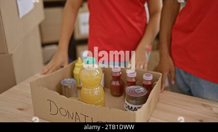 Deux jeunes et beaux bénévoles, homme et femme, travaillant ensemble, mettant des produits dans un paquet pour les dons dans un centre de charité, incarnant le sp Banque D'Images