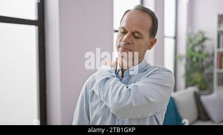 Homme hispanique d'âge moyen, l'air cool mais sérieux, souffrant de douleurs intenses à l'épaule à l'intérieur - un adulte, stressé par sa blessure, debout fort Banque D'Images