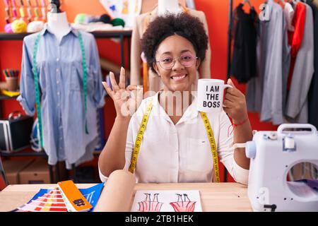 Belle femme africaine avec couturière frisée de cheveux buvant de je suis la tasse de patron faisant ok signe avec les doigts, souriant amicale gesturing exc Banque D'Images