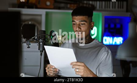 Jeune homme latin sérieux, musicien tatoué lisant sa chanson sur une partition, chantant son cœur dans un studio de musique faiblement éclairé Banque D'Images