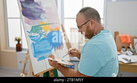 Bel homme caucasien d'âge moyen, un artiste profondément concentré alors qu'il dessine passionnément un portrait dans son atelier d'art intérieur Banque D'Images