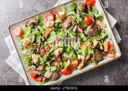 Délicieuse salade diététique de foie de poulet, roquette, oignons, tomates, croûtons et bacon gros plan dans une assiette sur la table. Vue de dessus horizontale depuis abo Banque D'Images