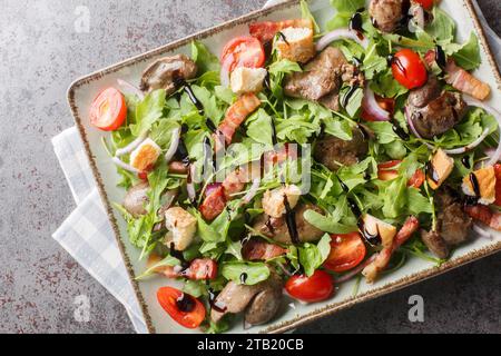 Apéritif de salade saine de foie de poulet frit, roquette, oignons, tomates, croûtons et bacon gros plan dans une assiette sur une table. Vue de dessus horizontale à partir de Banque D'Images