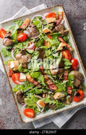 Salade de foie de poulet chaude avec bacon, tomates cerises, roquette. gros plan oignon rouge et croûtons sur l'assiette sur la table. Vue verticale de dessus Banque D'Images