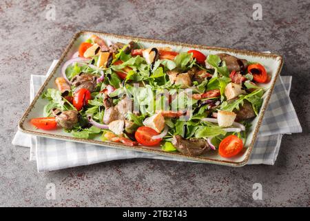 Apéritif de salade saine de foie de poulet frit, roquette, oignons, tomates, croûtons et bacon gros plan dans une assiette sur une table. Horizontal Banque D'Images