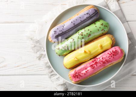 Eclairs frais citron, pistache, framboise et myrtille gros plan sur une assiette sur une table en bois. Vue de dessus horizontale Banque D'Images