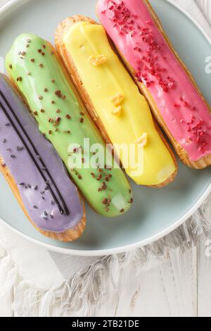 Délicieux éclairs colorés avec des saveurs de baies gros plan sur une assiette sur une table en bois. Vue verticale de dessus Banque D'Images