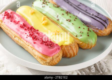 Eclairs frais citron, pistache, framboise et myrtille gros plan sur une assiette sur une table en bois. Horizontal Banque D'Images