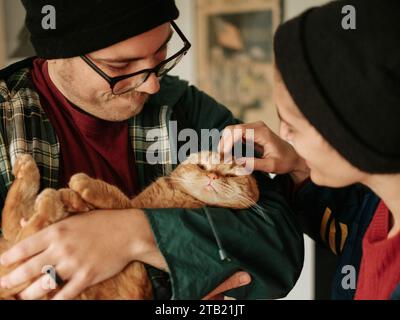 Couple douillet dans des bonnets, tenant et caressant un F écossais orange Banque D'Images