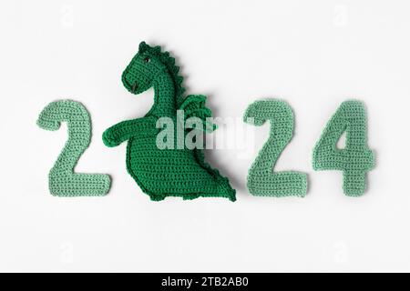 Jouet tricoté dragon vert et numéros verts tricotés. Le symbole de l'année 2024 sur fond gris. Banque D'Images