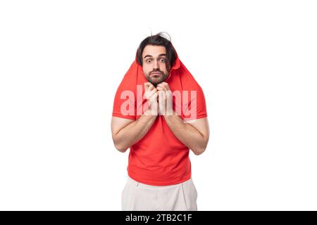 Un jeune européen de 35 ans avec une coupe de cheveux stylée et une barbe vêtu d'un t-shirt rouge se cache en mettant un t-shirt sur sa tête Banque D'Images