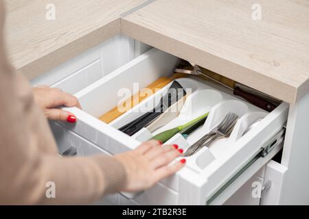 la main de la femme ouvre un tiroir de cuisine avec des couverts. la main féminine ouvre l'armoire de cuisine avec des ustensiles. tiroir avec ustensiles de cuisine. Banque D'Images