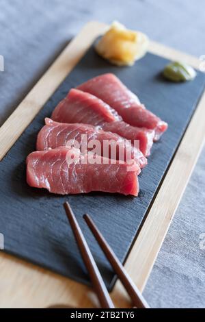 Cuisine maison de style japonais - sashimi de thon Akami cru maison sur une planche de service en ardoise avec baguettes en bois, gingembre et wasabi. ROYAUME-UNI Banque D'Images