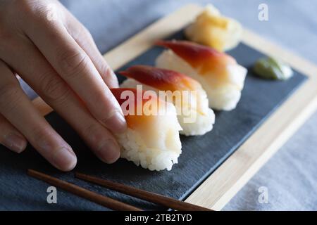 Femme asiatique plaçant un morceau de palourde surf de haute qualité (japonais : Hokkigai ou Ubaggai) sushi sur une planche d'ardoise. Préparation culinaire maison de style japonais Banque D'Images