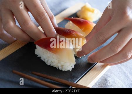 Femme asiatique plaçant un morceau de palourde surf de haute qualité (japonais : Hokkigai ou Ubaggai) sushi sur une planche d'ardoise. Préparation culinaire maison de style japonais Banque D'Images