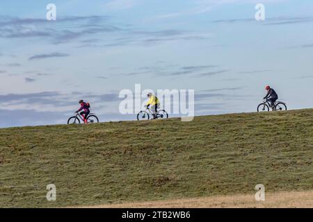 3 cyclistes dans la distance chevauchant autour du bord de la washland, Northamppon, Angleterre, Royaume-Uni Banque D'Images