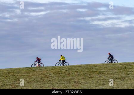 3 cyclistes dans la distance chevauchant autour du bord de la washland, Northamppon, Angleterre, Royaume-Uni Banque D'Images
