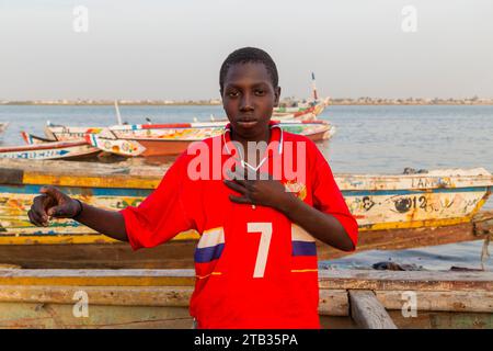 Dakar, Sénégal - 28 janvier 2019 : Portrait d'un jeune pêcheur contre son bateau sur le rivage Banque D'Images