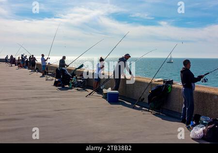 Les gens utilisant des cannes pour pêcher sur la jetée au port à Folkestone Kent Angleterre Royaume-Uni avec ciel bleu au-dessus. Banque D'Images