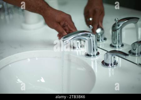 Homme ouvrant un robinet d'évier avec de l'eau chaude sortant du robinet Banque D'Images