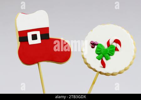 Biscuits de Noël POPS, l'un avec le motif de botte du Père Noël, l'autre avec le motif de canne à sucre, mis en valeur sur fond gris clair. Paire de biscuits festifs o Banque D'Images