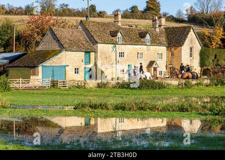 Les cavaliers passant devant Stowell Mill (ou Yanworth Mill) se reflètent dans les eaux de crue de la rivière naissante Coln près du village Cotswold de Yanworth, Glos. Banque D'Images