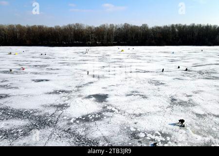 Un drone survole une rivière gelée en hiver. Les pêcheurs attrapent des poissons sur la belle glace bleue sur la rivière, lac en hiver, vue de dessus. Banque D'Images