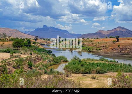 Rivière coulant à travers le paysage rural avec des montagnes lointaines dans la région de haute Matsiatra, hauts plateaux centraux, Madagascar, Afrique Banque D'Images