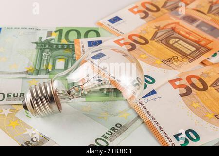 Une ampoule repose sur une table recouverte d'une grande quantité de billets en euros sur fond clair en gros plan Banque D'Images
