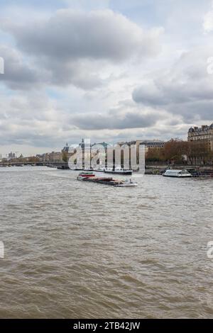 Paris, France, 2023. Une barge naviguant vers l'aval sur la Seine vue du Pont de la Concorde, avec le Musée d'Orsay en arrière-plan (vertical) Banque D'Images