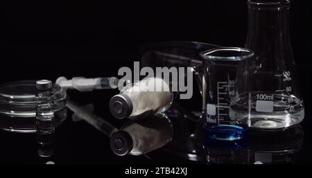 Equipement de laboratoire : seringue et médecine, tubes à essai et flacons tournant sur fond noir. Banque D'Images
