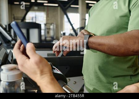 Homme noir inconnu regardant sa montre avec une autre personne caucasienne tenant son smartphone en main Banque D'Images
