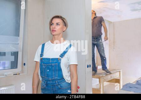 Les travailleurs font des réparations dans un nouvel appartement. Femme et homme plâtre murs et plafonds. Photo de haute qualité Banque D'Images