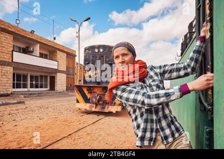 Jeune femme posant devant un vieux wagon ou une locomotive diesel à la gare vide abandonnée de Wadi Rum Banque D'Images