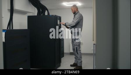 L'ingénieur professionnel ou le technicien portant l'uniforme utilise l'ordinateur tablette. L'inspecteur masculin vérifie et surveille le système d'alimentation à l'usine ou à l'installation énergétique. Spécialiste industriel travaille dans une usine moderne. Banque D'Images